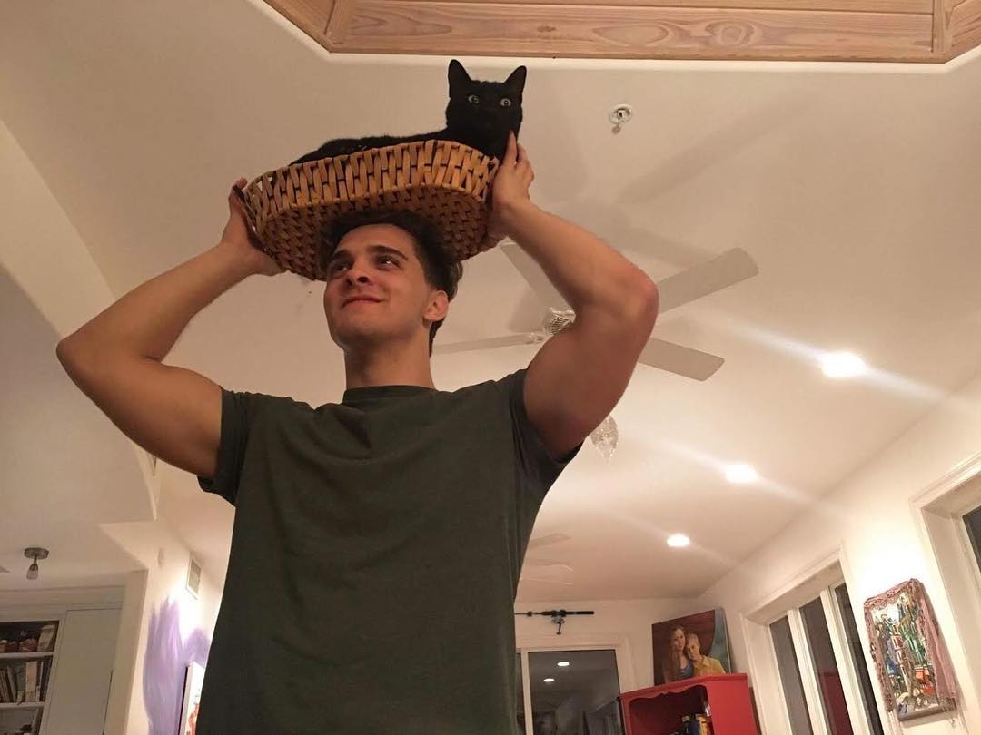 John with a cat in a basket on his head.